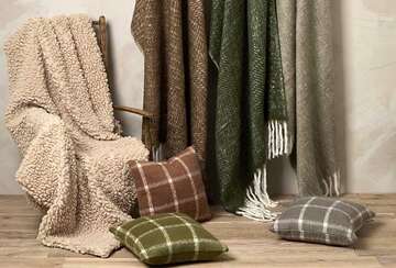 Cosy Faux Shearling Throw draped over a chair, surrounded by decorative cushions in earthy tones.