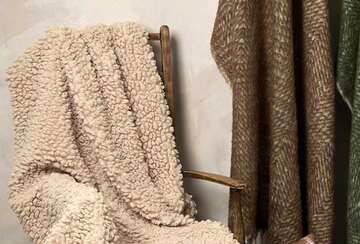 Cosy Faux Shearling Throw draped over a wooden chair, showcasing luxurious texture and natural linen color.