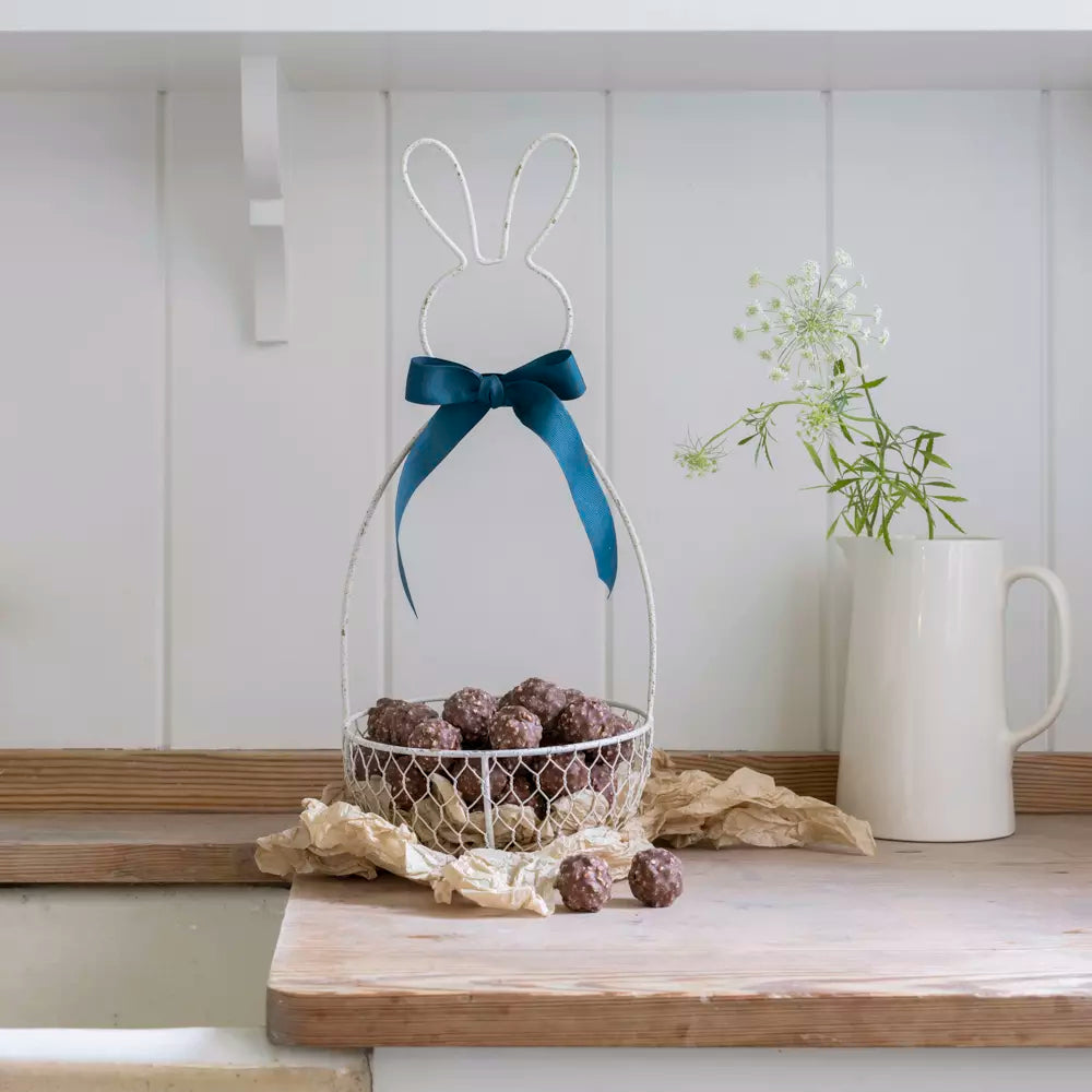 Metal Bunny Basket - Antique White with chocolate treats and decorative ribbon in a charming kitchen setting.