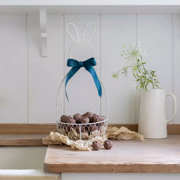 Metal Bunny Basket - Antique White with chocolate treats and decorative ribbon in a charming kitchen setting.