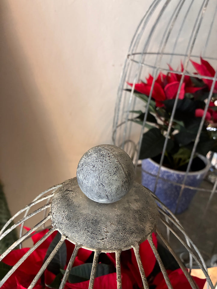 Close-up of the top of a bird cage style plant stand on legs, showcasing its vintage silvery grey finish and decorative accents.
