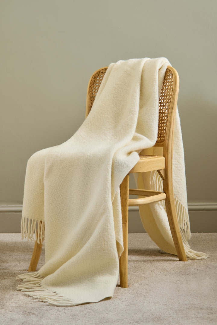 The Moorland - Cream Wool Throw draped over a wooden chair, adding cosy home charm to the Devon decor.