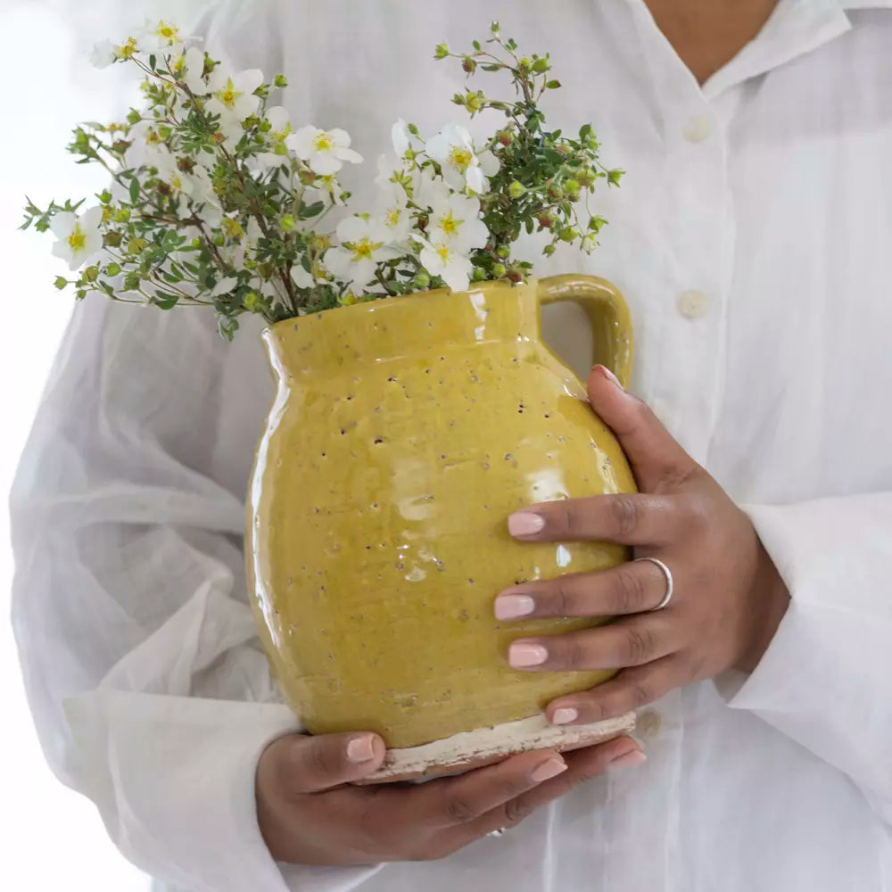 Mustard Yellow Rustic Glazed Jug with fresh flowers, holding by a person in a white shirt, perfect for decor and use.