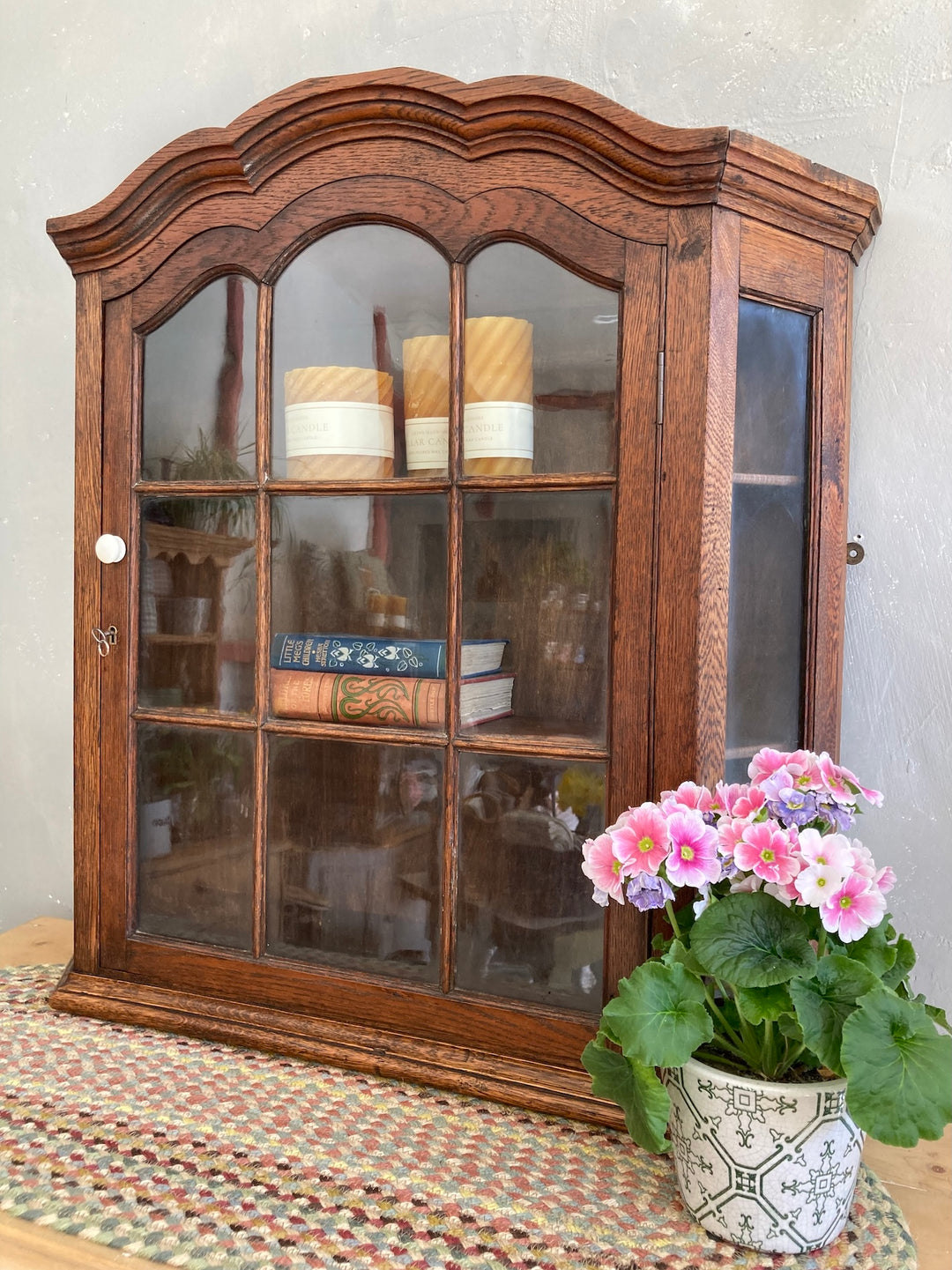 Antique oak wall cabinet with glass door, featuring Dutch influence and decorative porcelain knob.