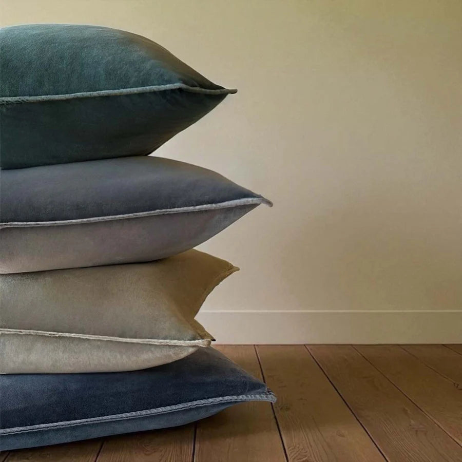 Stonewashed velvet cushions in various earthy shades stacked on a wooden floor, perfect for home decor from Source for the Goose, Devon.