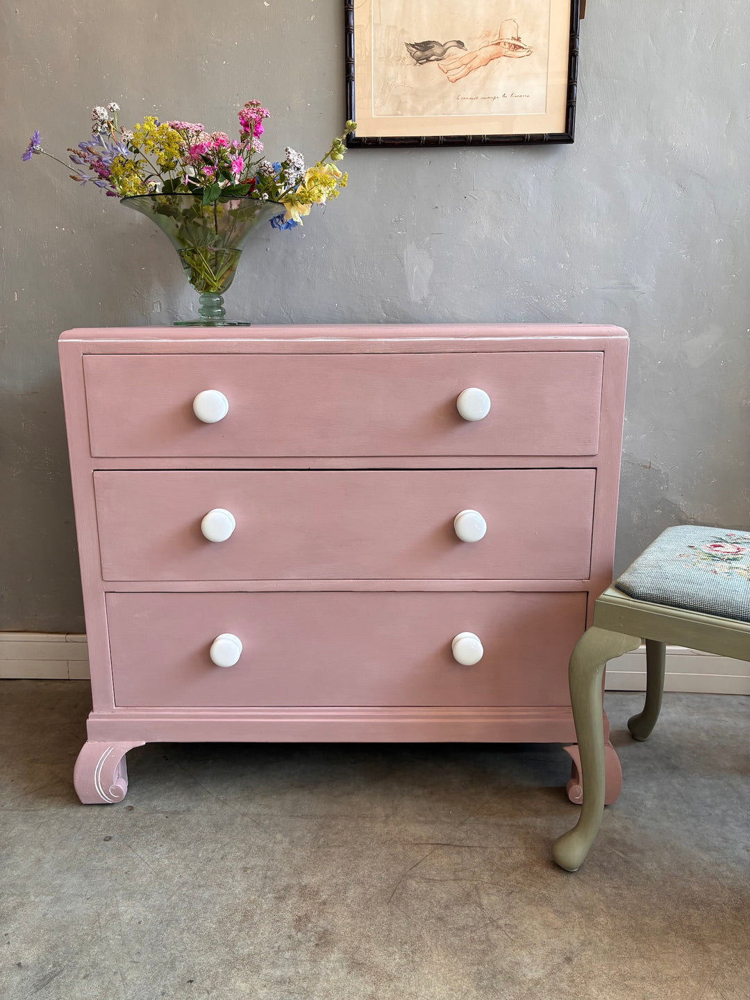 Pink Chest of Drawers with Porcelain Handles displayed with flowers and a decorative chair.