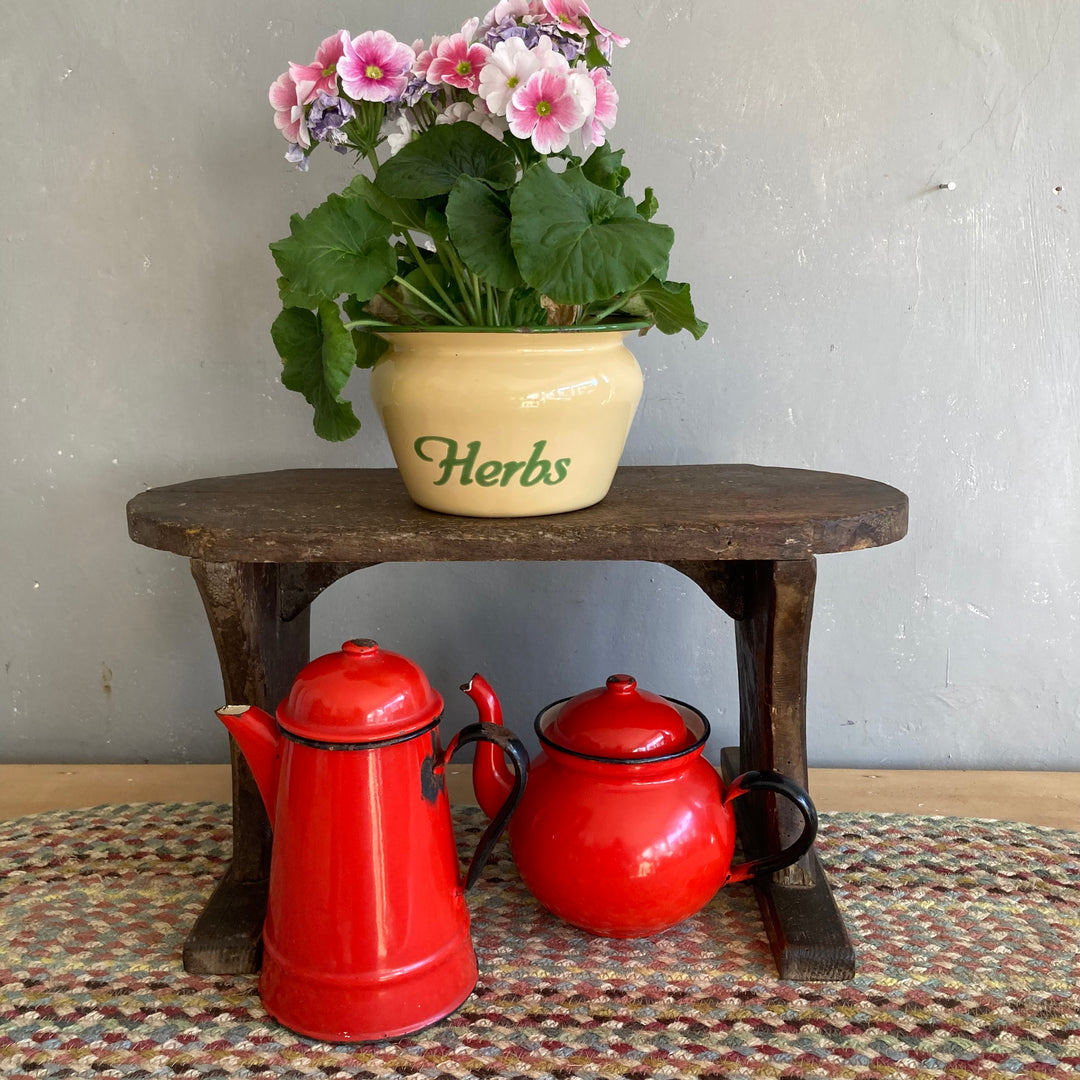 Vintage red enamel tea and coffeepot on rustic table with herb pot and flowers, perfect for country kitchen decor.