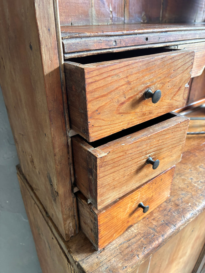 Rustic Antique Pine Dresser with visible wooden drawers showcasing aged finish and black metal knobs.