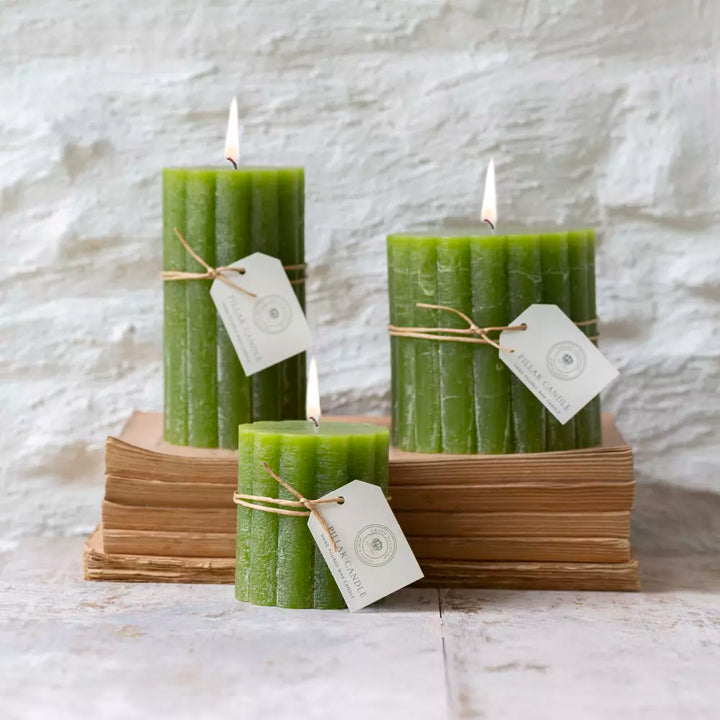 Rustic scalloped pillar candles in fern green, elegantly arranged on stacked books by Source for the Goose, Devon.