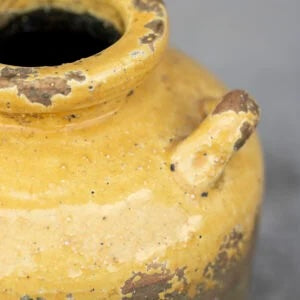 Close-up of a handcrafted rustic urn with yellow glaze, showcasing its terracotta texture and vintage charm.