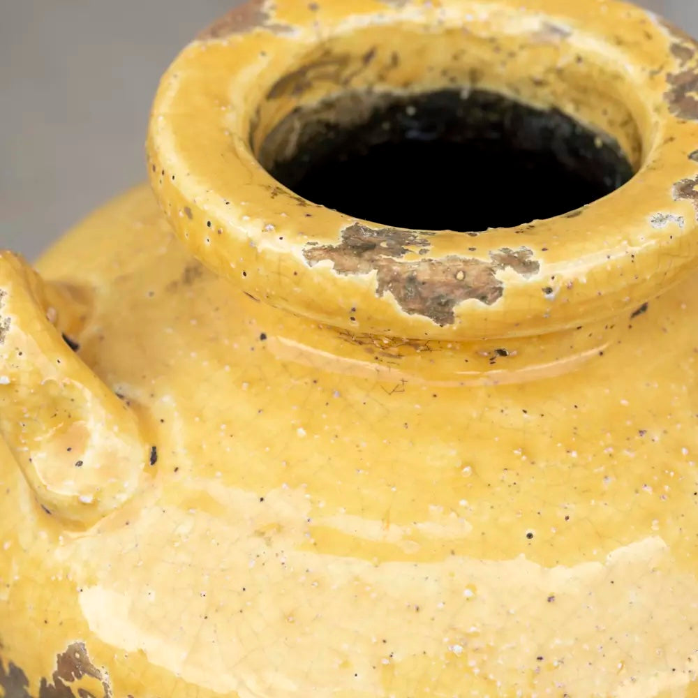 Close-up of rustic terracotta urn with bright yellow glaze, displaying weathered texture and Mediterranean charm.