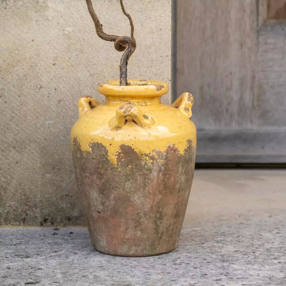 Handcrafted rustic urn with warm yellow glaze, showcasing a weathered terracotta look, perfect for home decor.