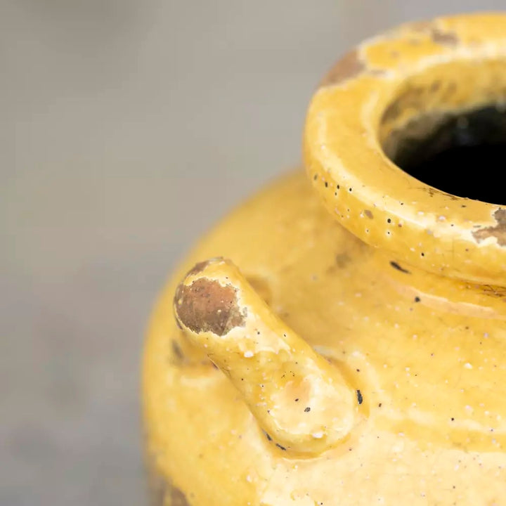 Close-up of a handcrafted rustic urn with a warm yellow glaze, highlighting its textured finish and unique shape.