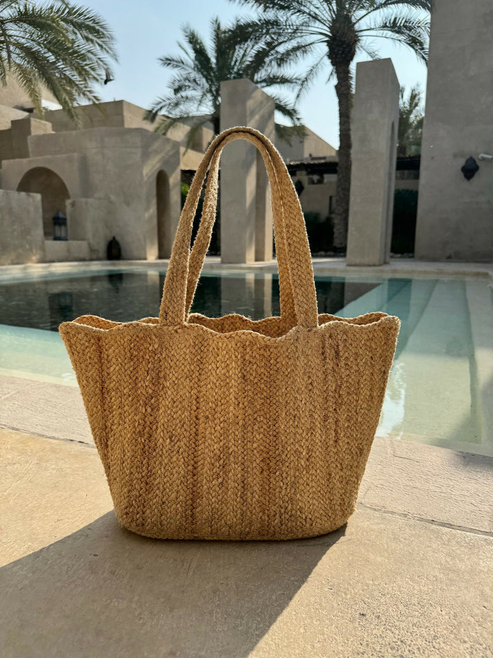 natural jute tote bag with scallop top being used a beach bag sat in front of a pool on holiday