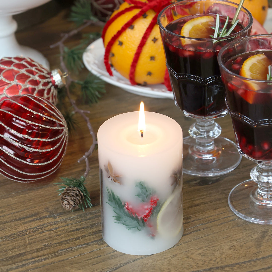Christmas Spice Pillar Candle with holly, surrounded by festive drinks and ornaments, perfect for holiday décor.