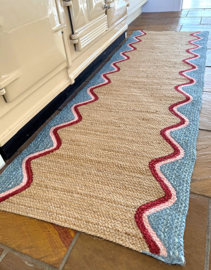 Sky Wave Organic Jute Braided Rug in a kitchen setting with a wave border design and soft pink trim.