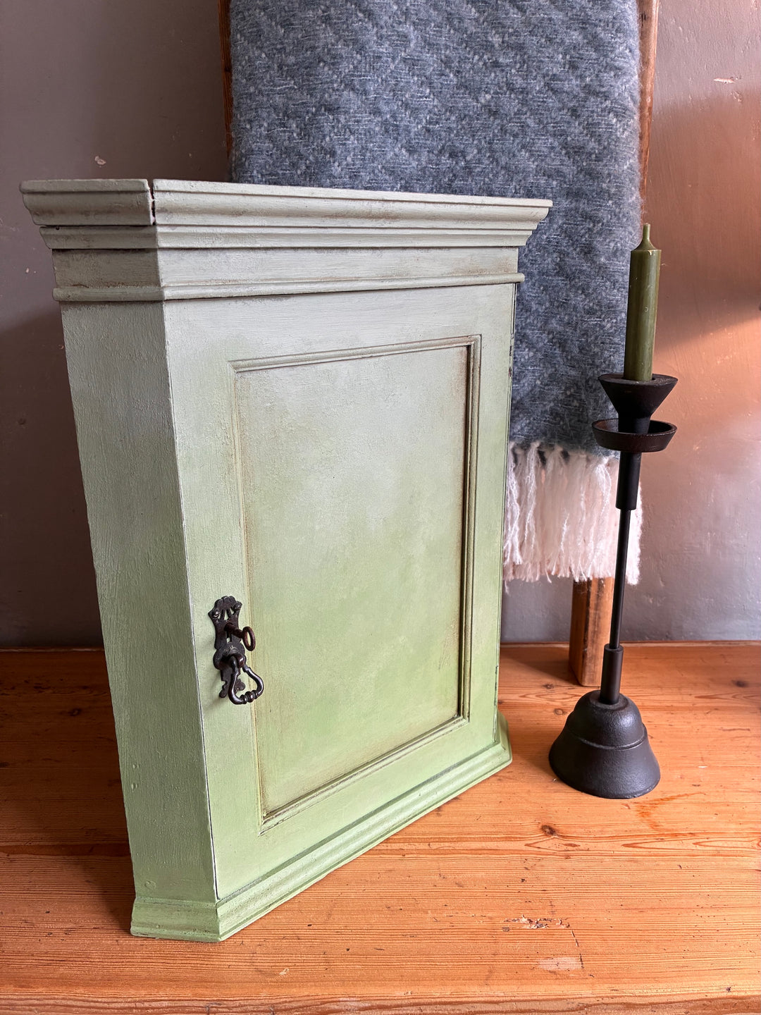 Green wooden cabinet on a wooden floor with a candle holder in the background.