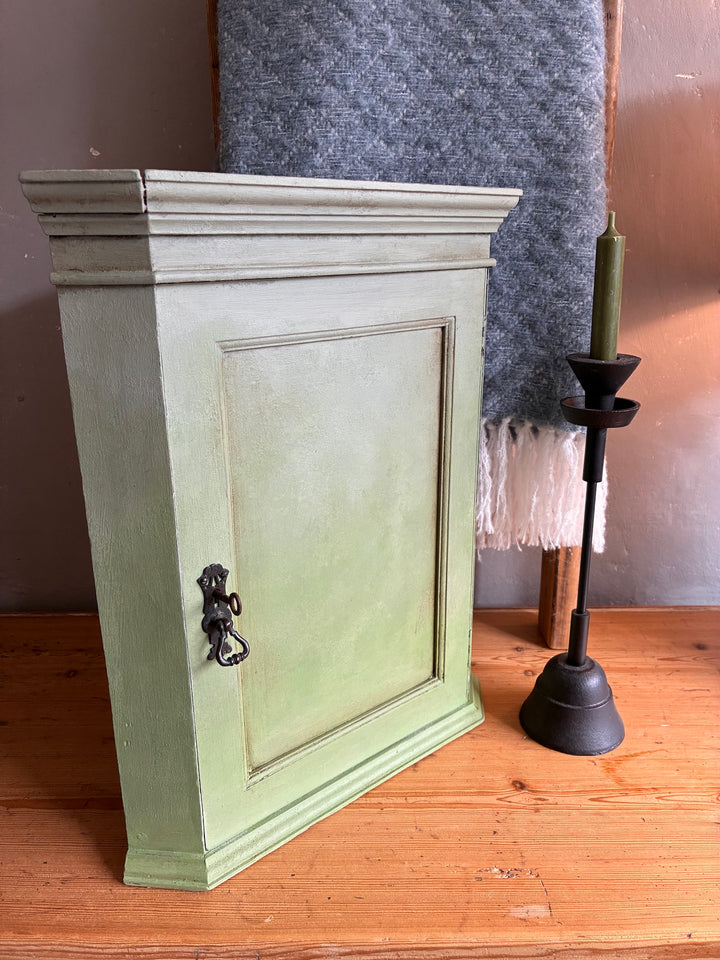 Green wooden cabinet on a wooden floor with a candle holder in the background.
