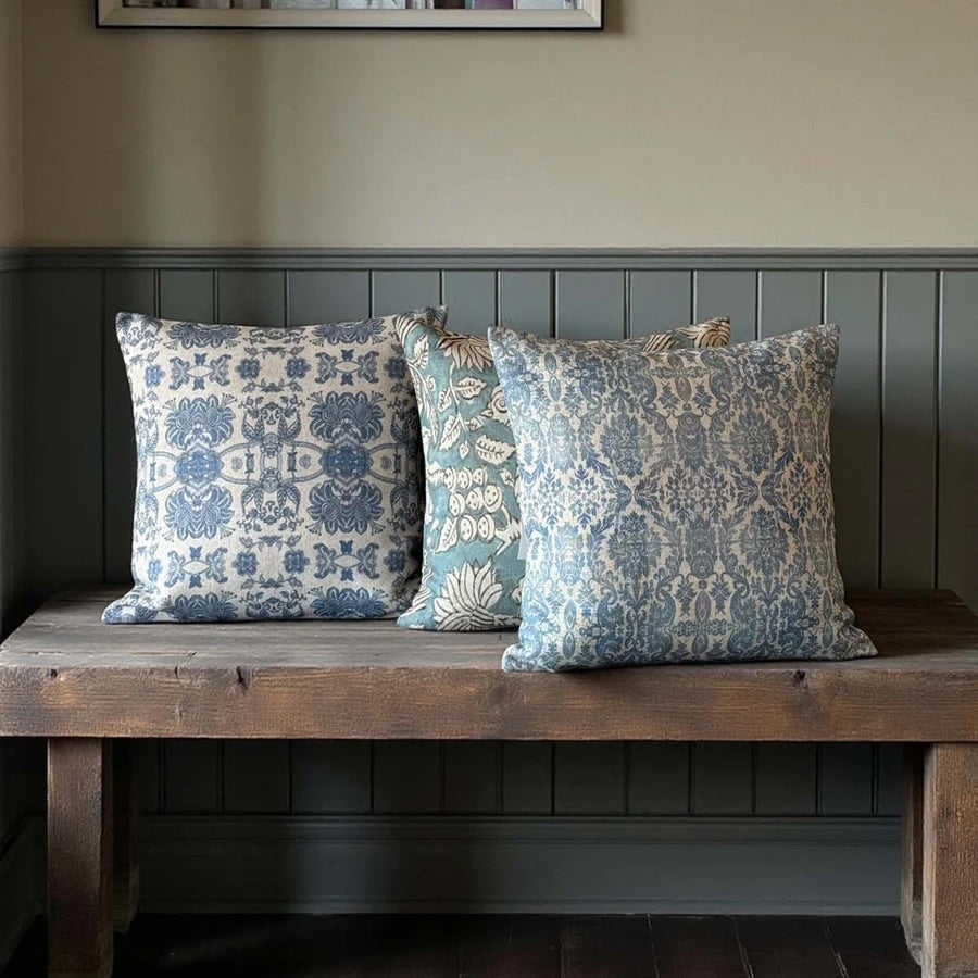 Softspell Wedgewood Blue Linen Mix Cushion on a rustic wooden bench with blue floral patterns.