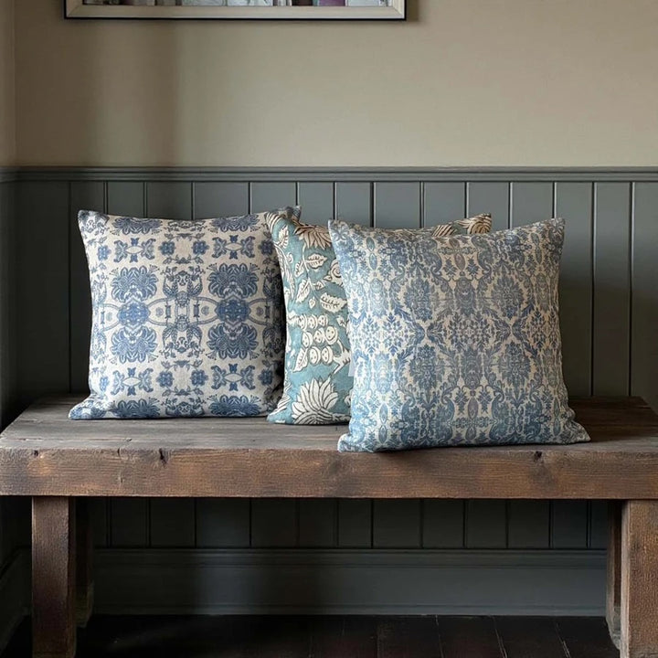 Softspell Wedgewood Blue Linen Mix Cushion on a rustic wooden bench with blue floral patterns.