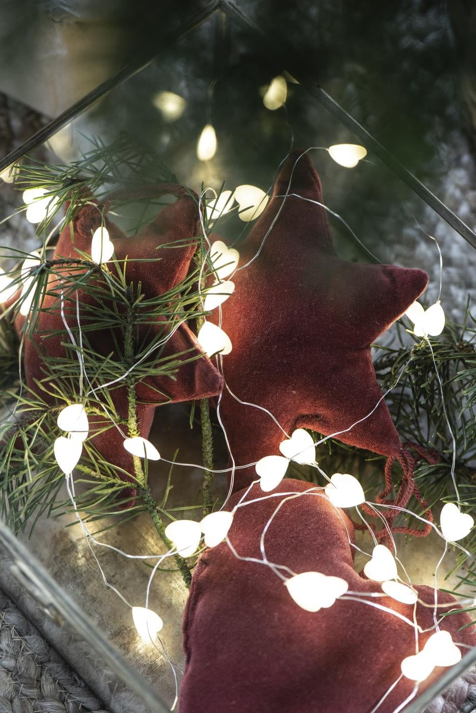 Warm String of Heart LED Lights entwined with festive greenery and soft star ornaments for Christmas decor.