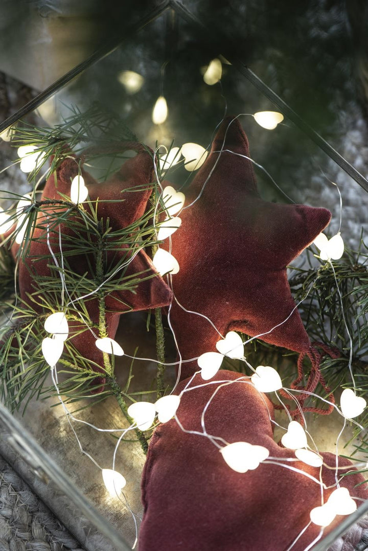 Warm String of Heart LED Lights entwined with festive greenery and soft star ornaments for Christmas decor.