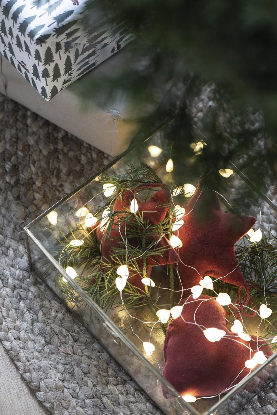 String of heart LED lights illuminating a decorative box with star-shaped cushions and greenery for Christmas decor.