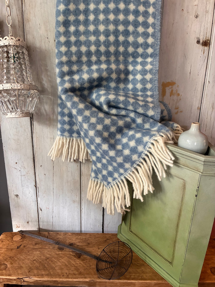 Blue and white checkered throw blanket draped over a wooden cabinet with a rustic background.