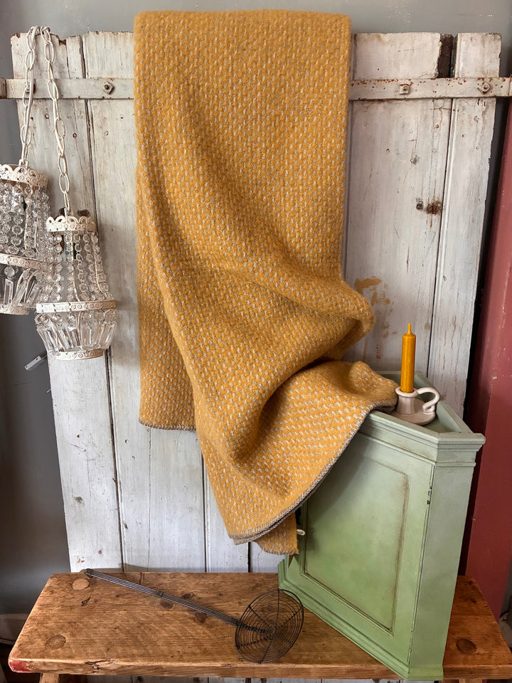 Mustard yellow blanket draped over a wooden cabinet against a rustic wooden wall.