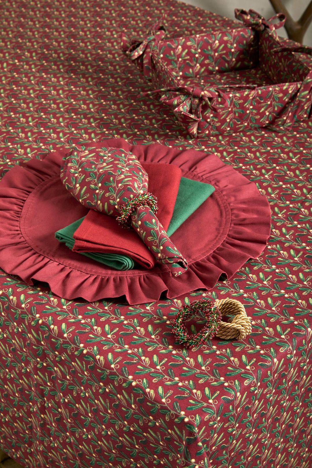 Under The Mistletoe Napkin - Set of Four displayed on a festive red tablecloth with mistletoe design.
