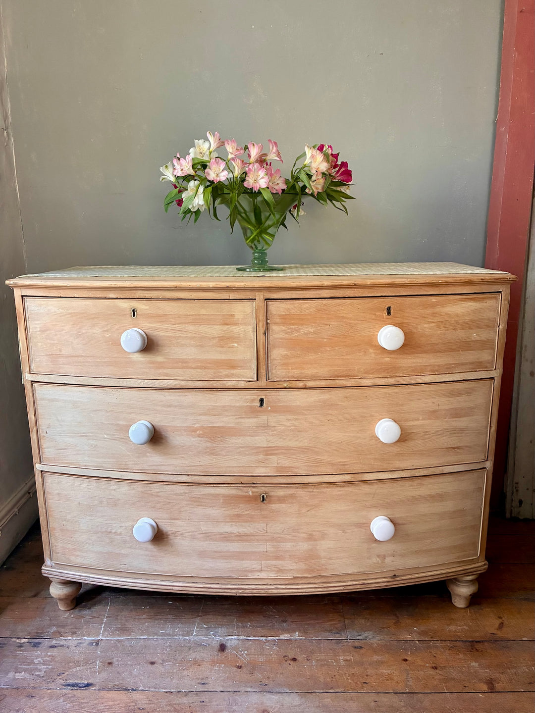 Antique Pine Bow Front Chest of Drawers showcasing elegant craftsmanship in a rustic home setting with flowers.