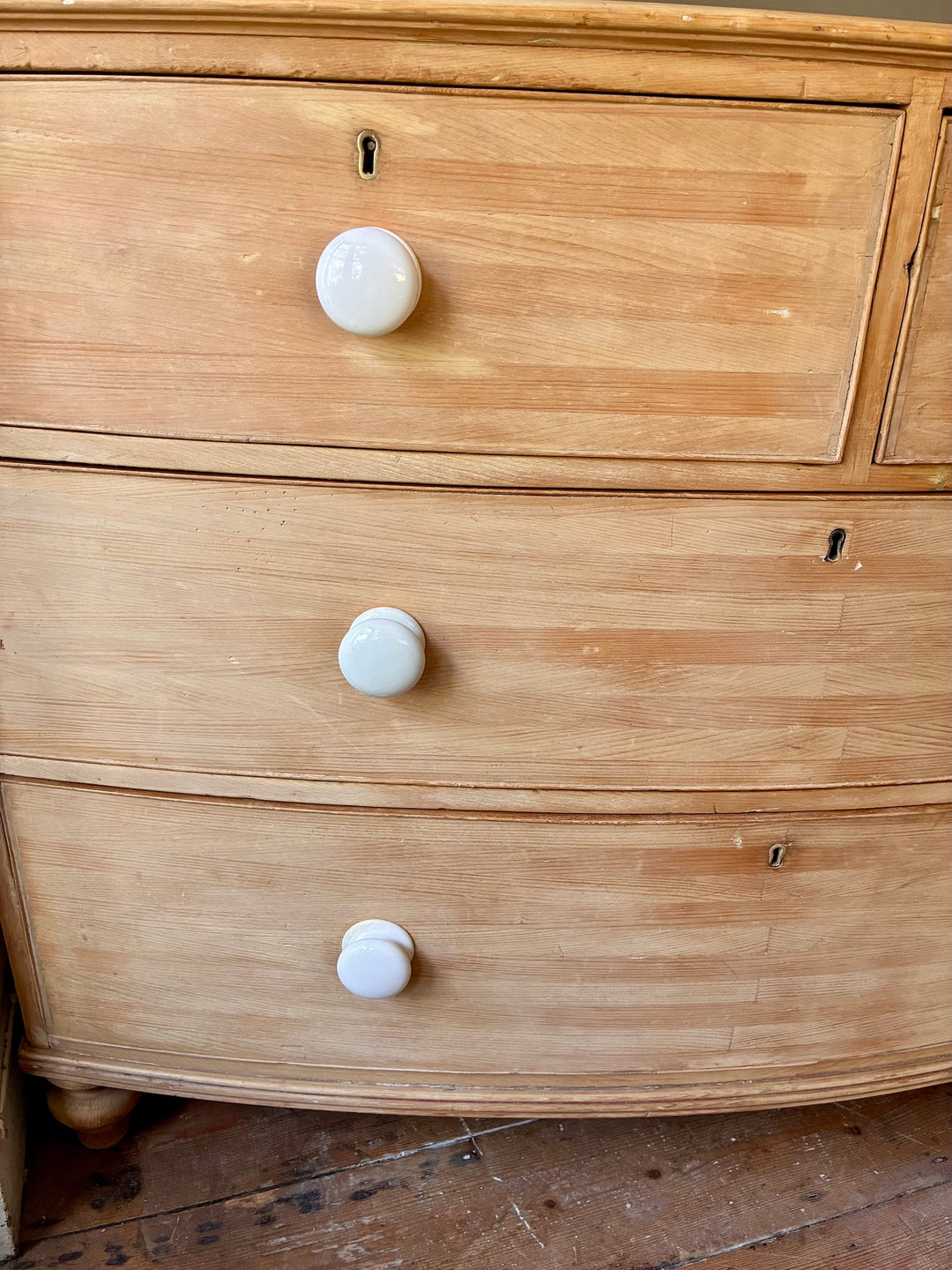 Antique Pine Bow Front Chest of Drawers featuring white porcelain handles and rustic craftsmanship.