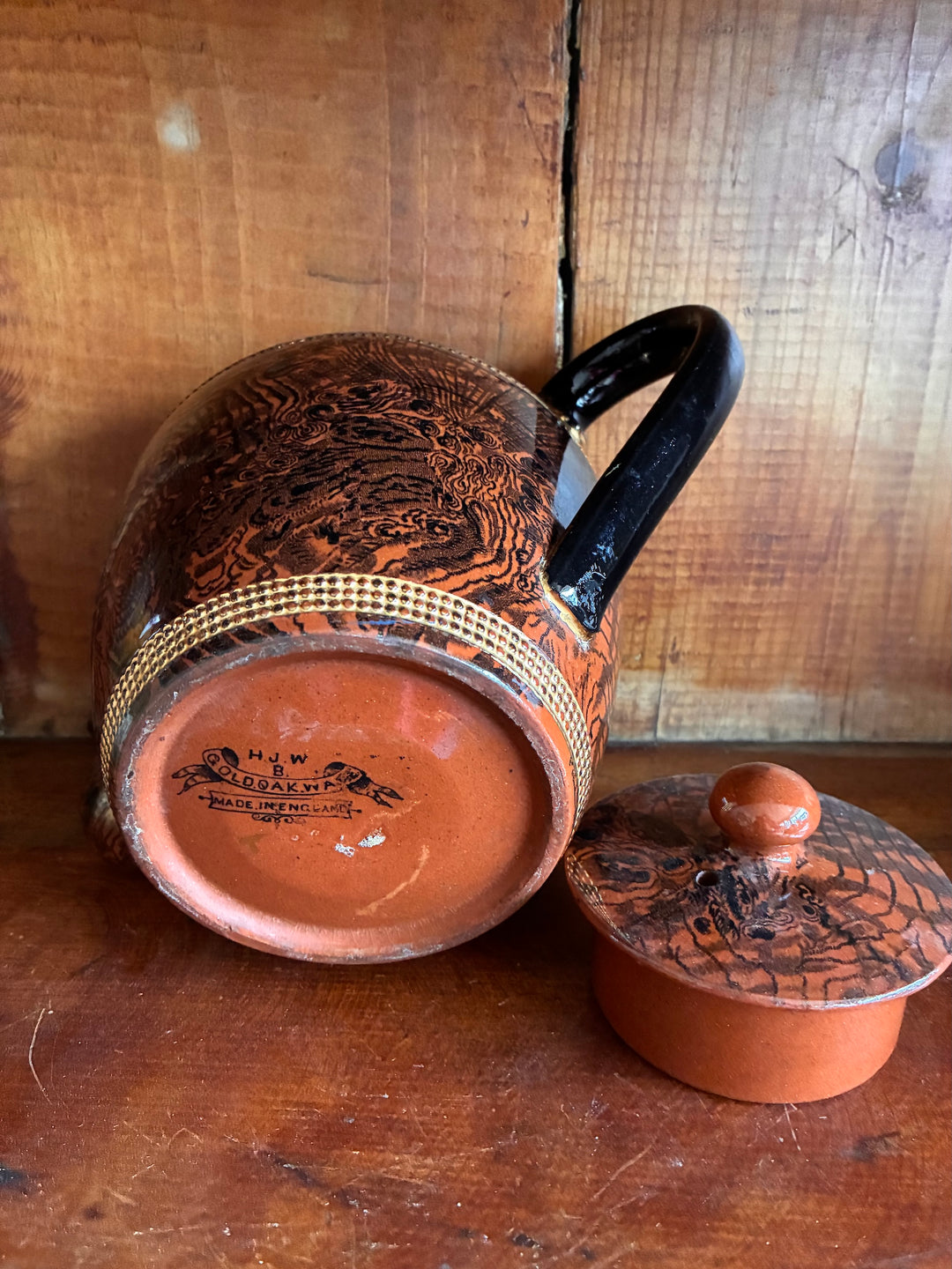 Vintage Oak Ware Design Brown Betty Teapot with bark-like pattern and gilt stripes on a wooden background.