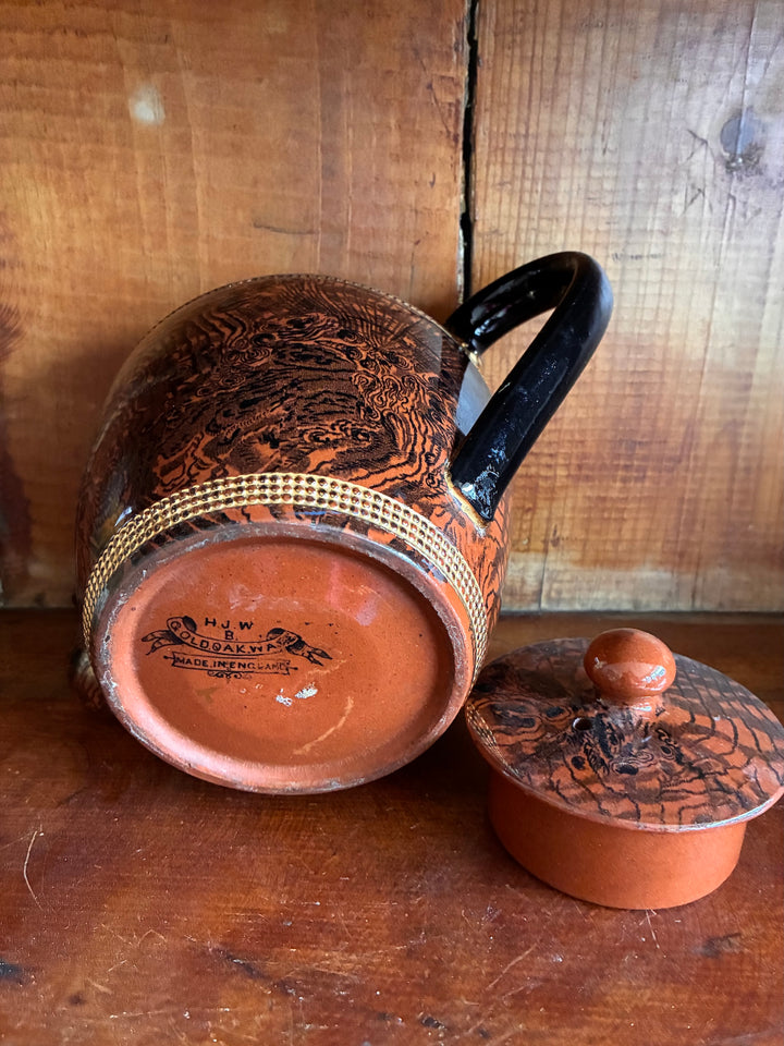 Vintage Oak Ware Design Brown Betty Teapot with bark-like pattern and gilt stripes on a wooden background.