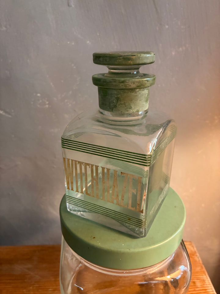 Vintage 1930s Glass Bathroom Set featuring a glass bottle labelled Witch Hazel with green lettering.