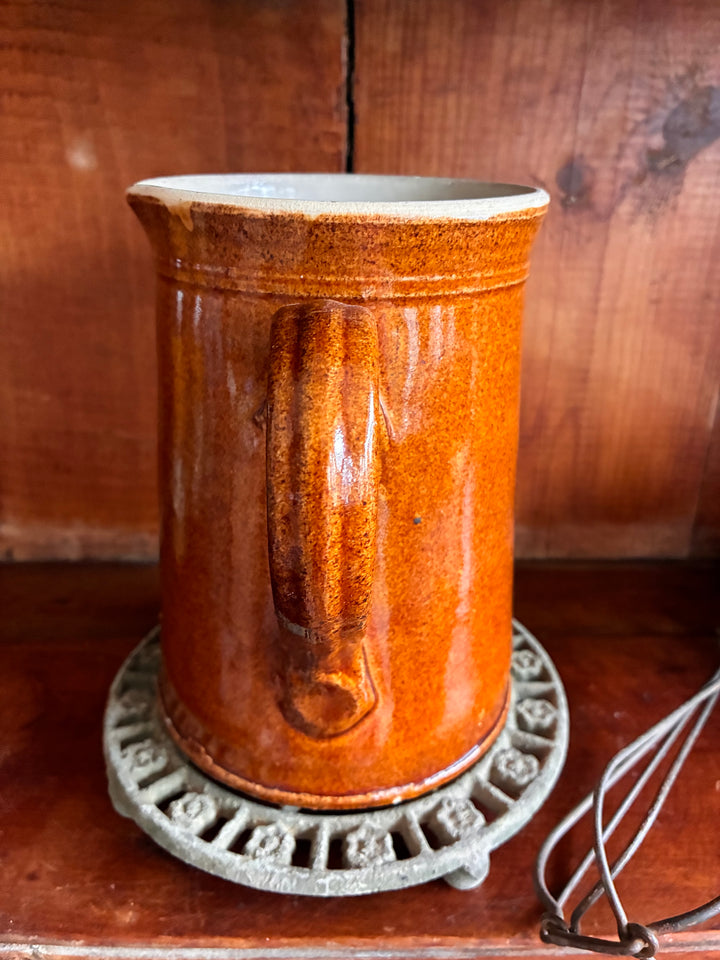 Antique French Earthenware Milk Pitcher with medium brown glaze and smooth interior on a decorative metal stand.
