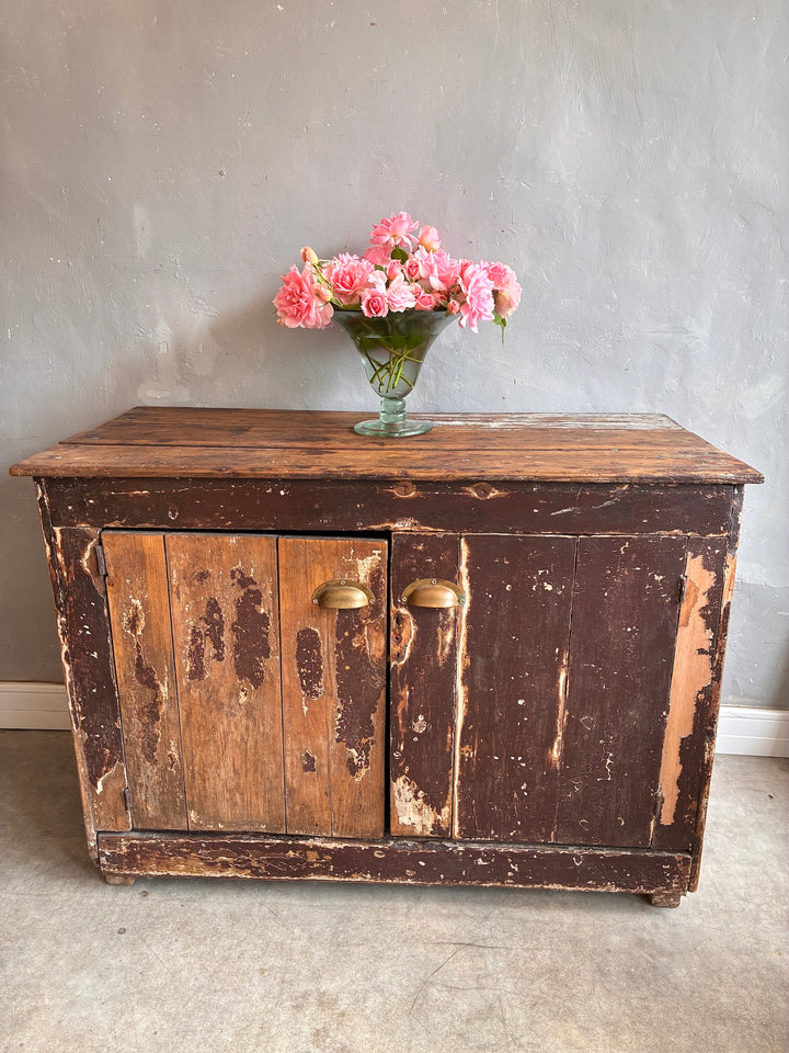 Primitive Antique Pine Wooden Sideboard with flowers on top against a gray wall, showcasing rustic charm and weathered textures.