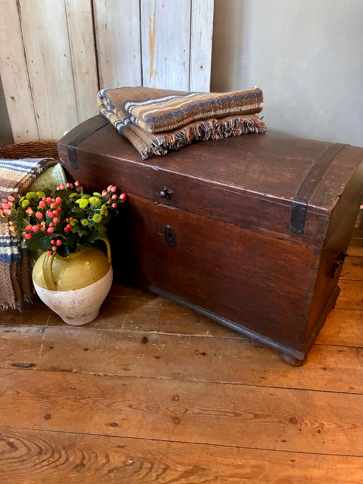 Antique Wooden Dome Top Trunk with flowers and blankets, showcasing rustic charm and vintage appeal.
