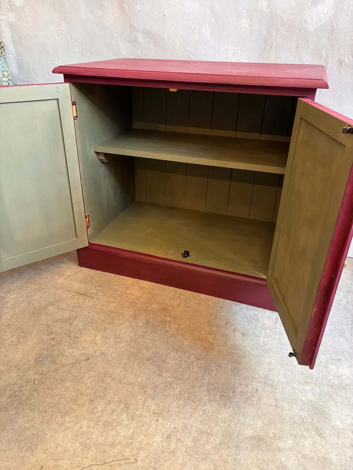 Open interior of an aubergine folk art style cupboard by Source for the Goose, featuring olive green shelves.