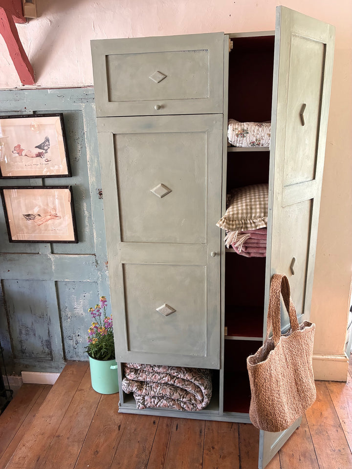 Tall Vintage Green Wooden Cupboard with multiple storage sections and a brick red interior, styled with cozy textiles.