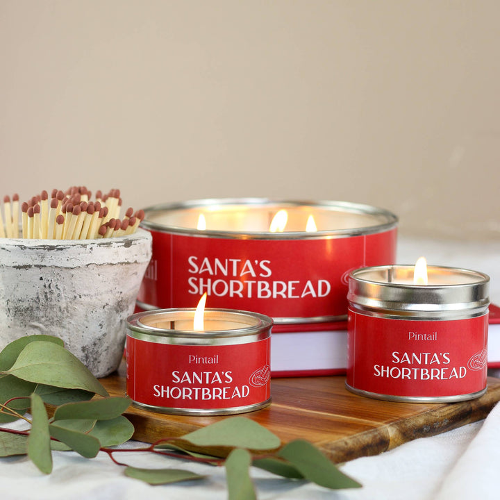 Santa's Shortbread Classic Tin Candle by Pintail Candles, lit and displayed with matches, offering a cosy festive atmosphere.