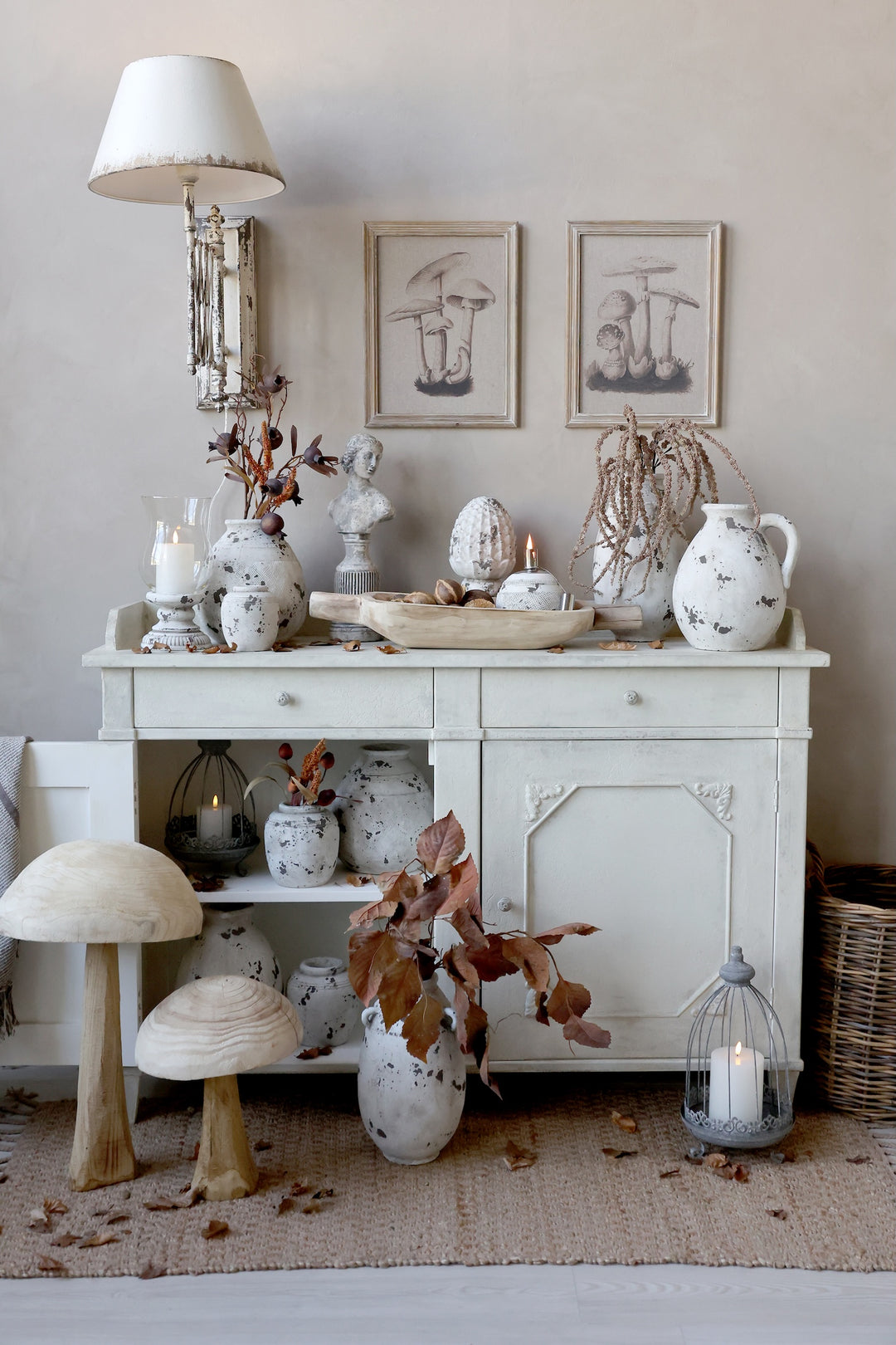 A vintage-inspired sideboard adorned with decorative busts, pottery, and autumn leaves, creating a charming home decor scene.