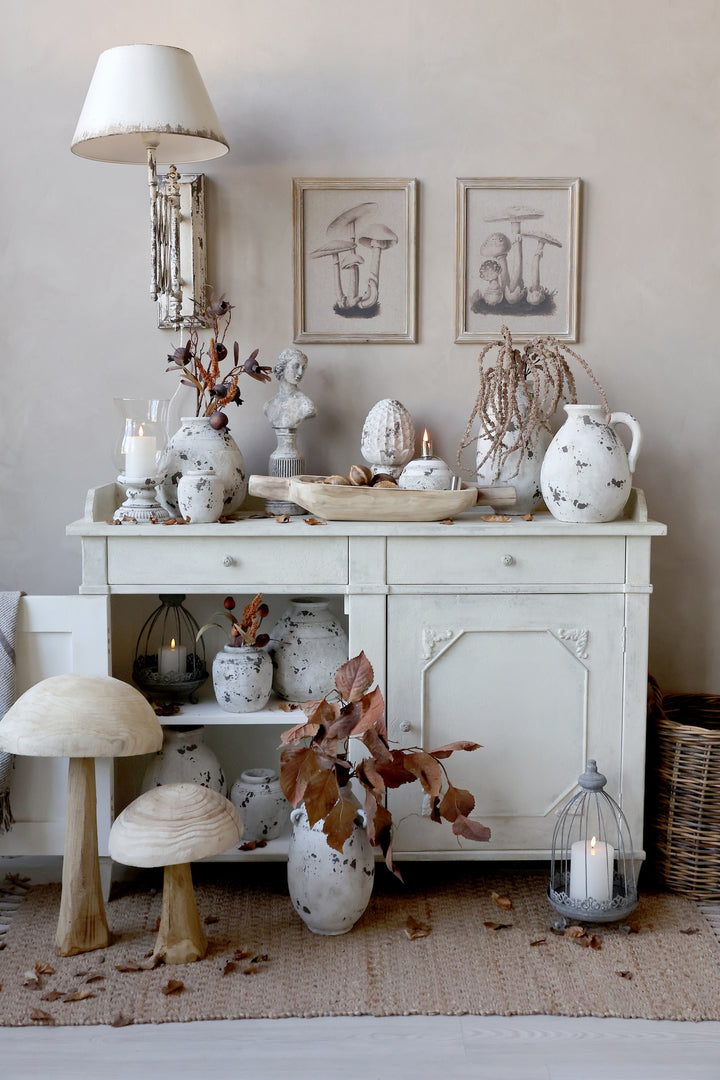 A vintage-inspired sideboard adorned with decorative busts, pottery, and autumn leaves, creating a charming home decor scene.