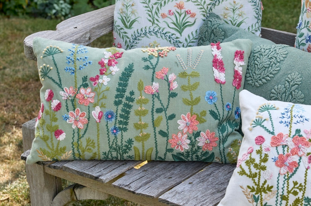 Grasmere Embroidered Cushion in Green on a wooden bench with floral designs, perfect for decor.
