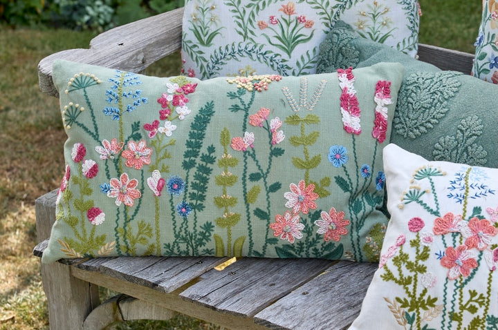 Grasmere Embroidered Cushion in Green on a wooden bench with floral designs, perfect for decor.