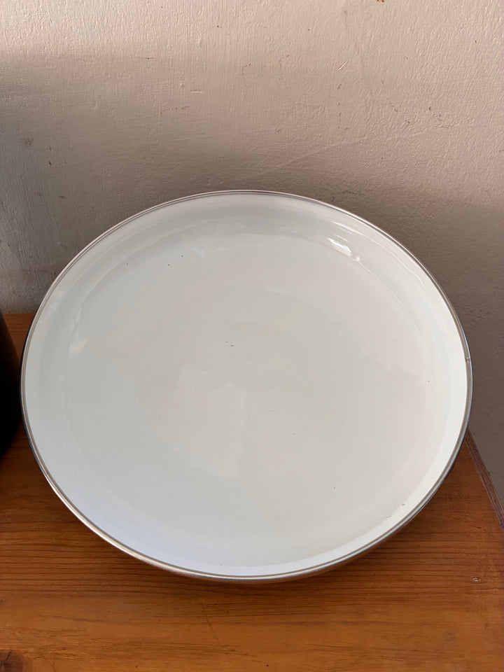 White enamel serving plate with silver rim, perfect for rustic kitchen decor.