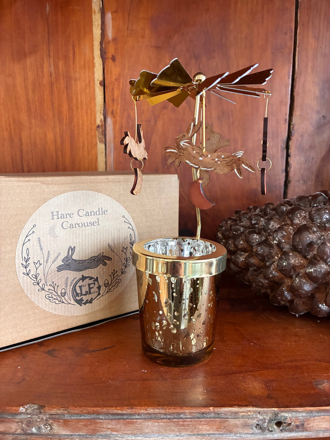 Hare Candle Carousel by Lily Faith – Spinning Christmas Tealight Holder on a wooden surface with box and pinecone.
