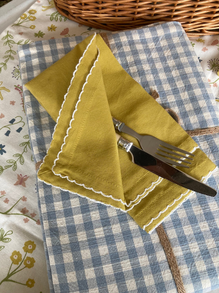 Set of four lemon yellow scallop napkins on a blue checkered tablecloth, perfect for summer dining.