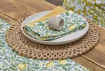 Round hand woven jute tablemat from Source for the Goose, featuring a chic design with green patterned napkins and plate.