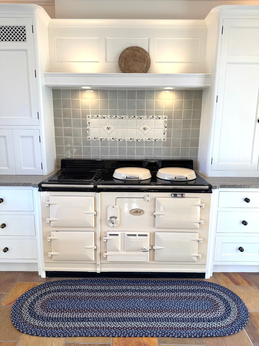 Lupin Blue Rectangle Organic Jute Braided Rug placed in a stylish kitchen with a cream stove and grey tiled backsplash.